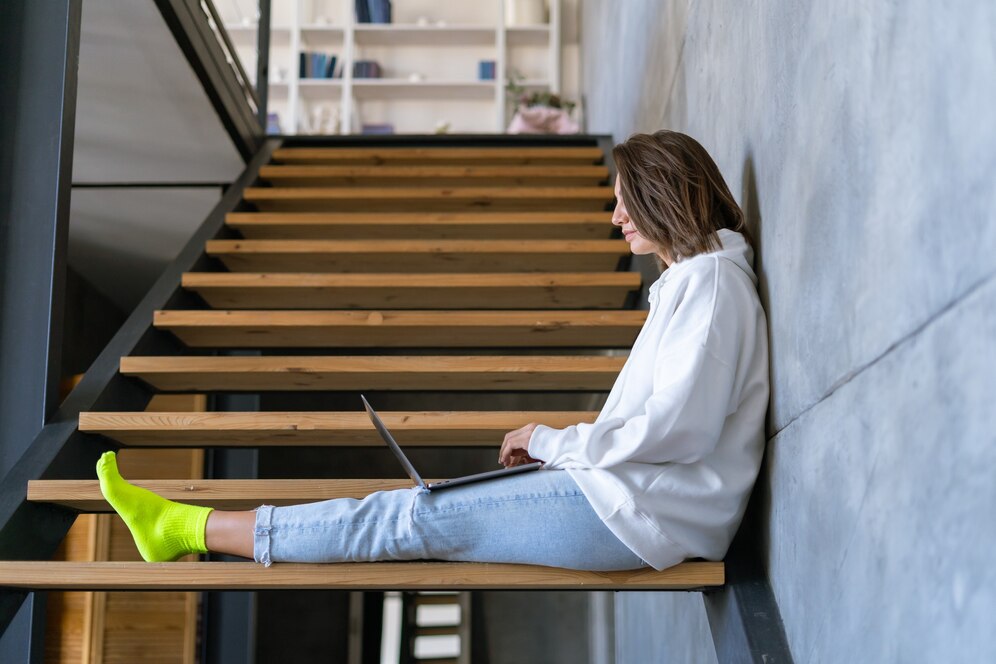 young-woman-home-white-hoodie-jeans-sits-stairs-with-laptop-her-knees_343596-7255